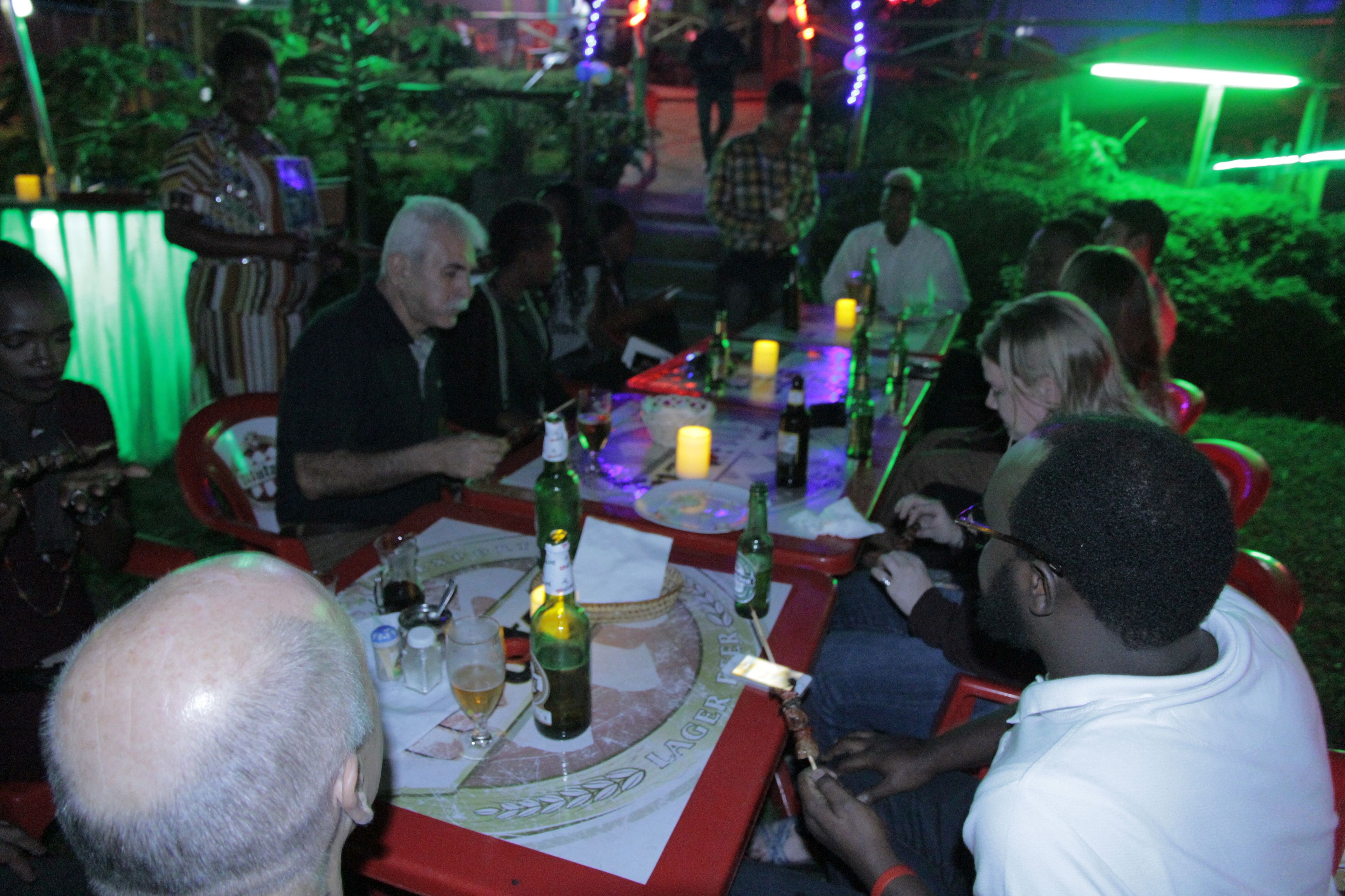 Un groupe de personnes est assis à une table à l’extérieur, avec des bouteilles et des verres, ce qui laisse supposer qu’il s’agit d’un rassemblement ou d’un événement social.
