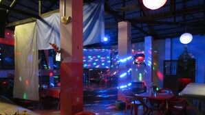 An indoor venue with tables and chairs, a stage with colorful lights, and a disco ball. - Colours Club Spa and Garden Resort (Kigali)