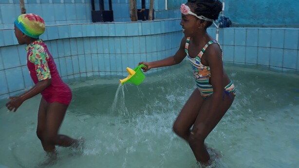 Two people playing in a water-filled area with tiled walls and a blue ceiling. - Colours Club Spa and Garden Resort (Kigali)