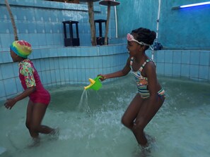 Two people playing in a water-filled area with tiled walls and a blue ceiling. - Colours Club Spa and Garden Resort (Kigali)