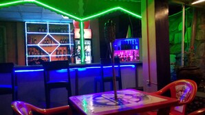 A bar area with neon lights, bar stools, and a table with a logo. - Colours Club Spa and Garden Resort (Kigali)