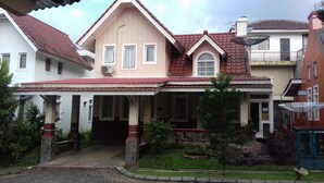 A two-story house with a red-tiled roof, a covered porch, and a stone foundation. - Kota Bunga R (Cipanas)
