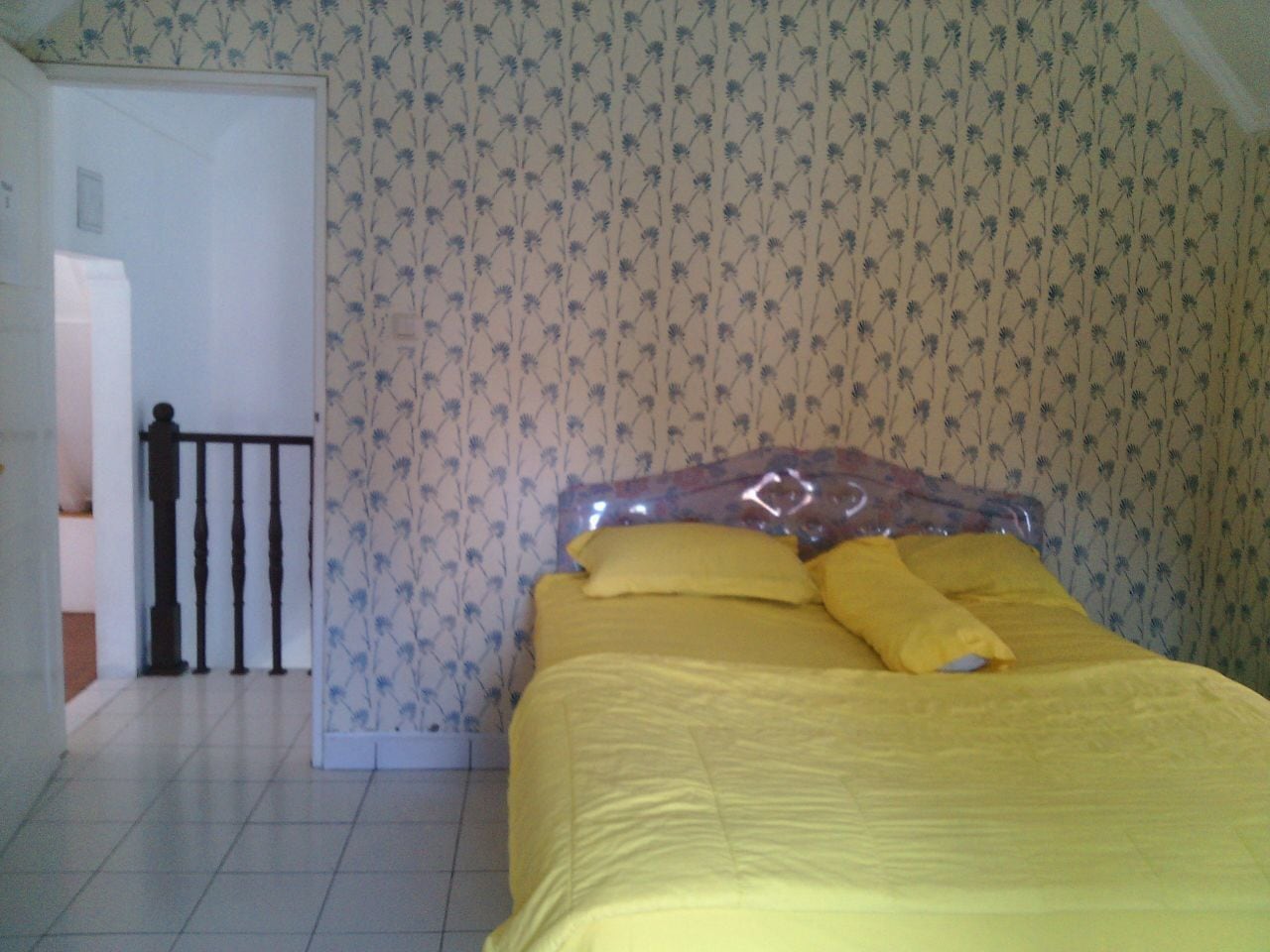 Un dormitorio con cama, una puerta y un papel tapiz estampado.