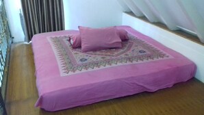 A bed with a pink bedspread and a decorative pillow, positioned against a wall with a window and curtains. - Kota Bunga R (Cipanas)