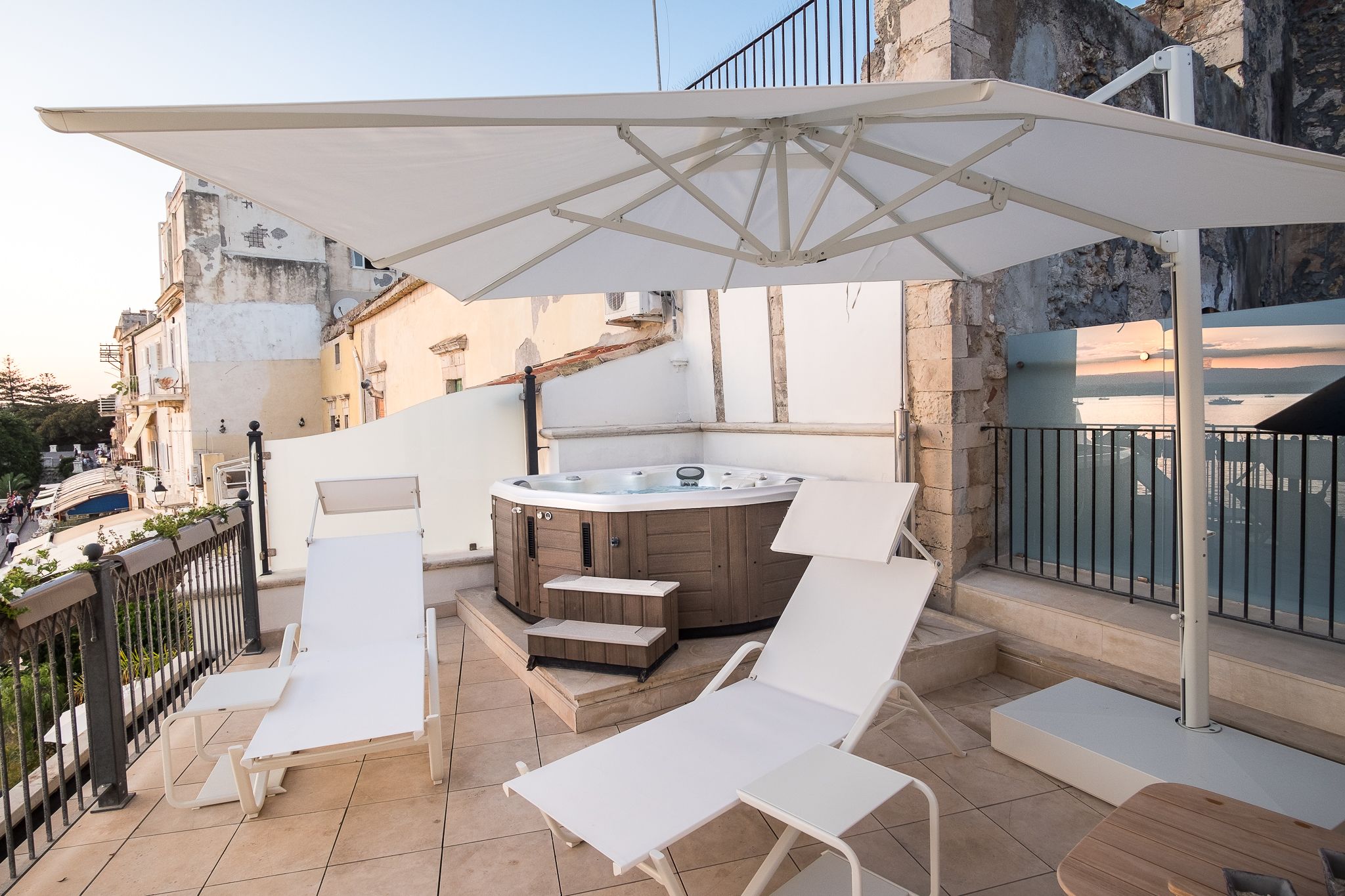 Eine Dachterrasse mit Whirlpool, weißen Liegestühlen und einem großen Sonnenschirm.