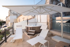 En tagterrasse med jacuzzi, hvide liggestole og en stor parasol.