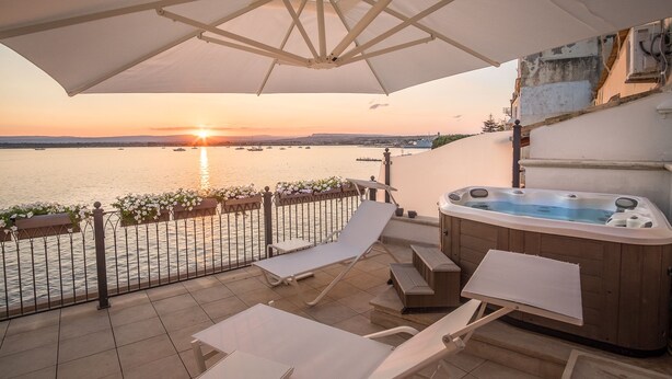 Ein Balkon mit Whirlpool, Liegestühlen und Blick auf den Sonnenuntergang über dem Wasser.