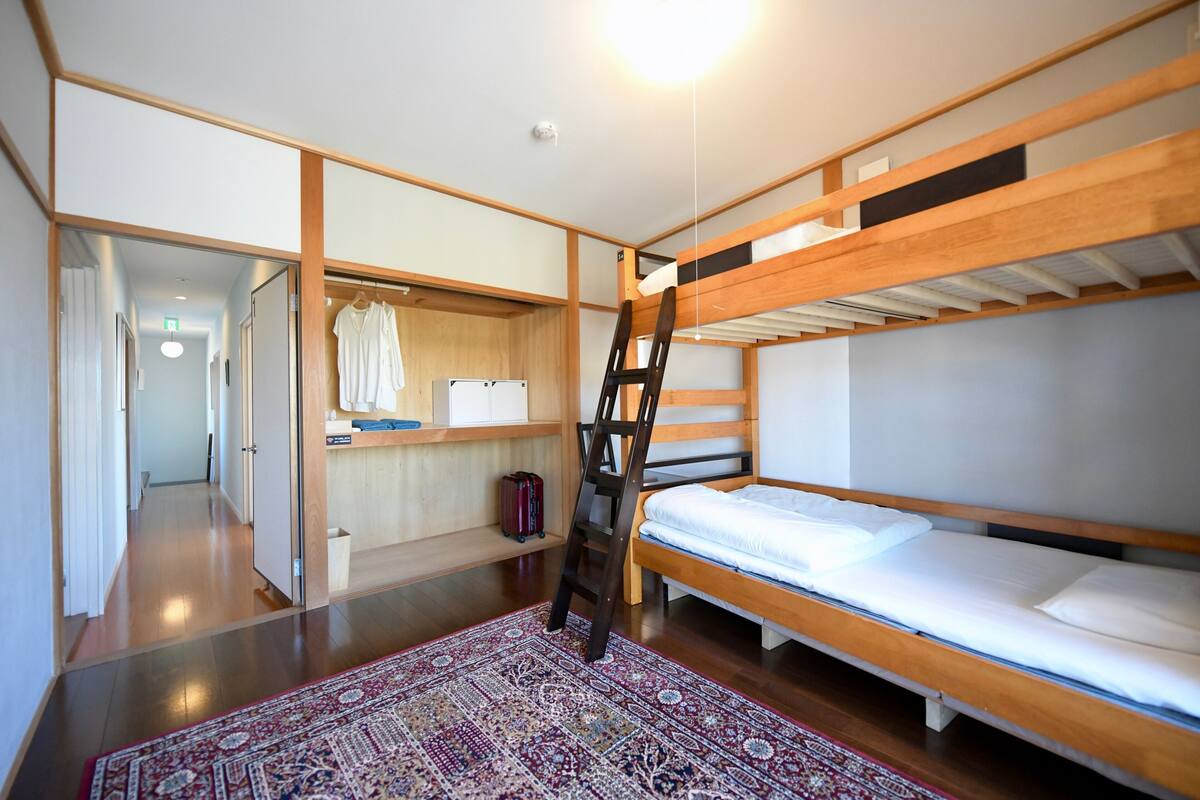 A bunk bed room with a ladder, a small desk, and a wardrobe.