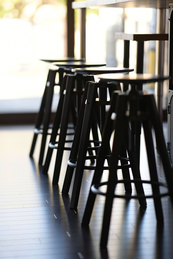 A row of black bar stools with a metal frame, arranged in a line along a wooden floor, leading to a table with a white top. - Ise Guest House sora - Hostel (Ise)