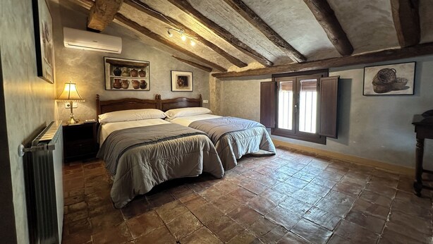 A rustic bedroom with two beds, a radiator, a lamp, and a shelf with pottery. - Casa Rural La Cuca (Lerín)