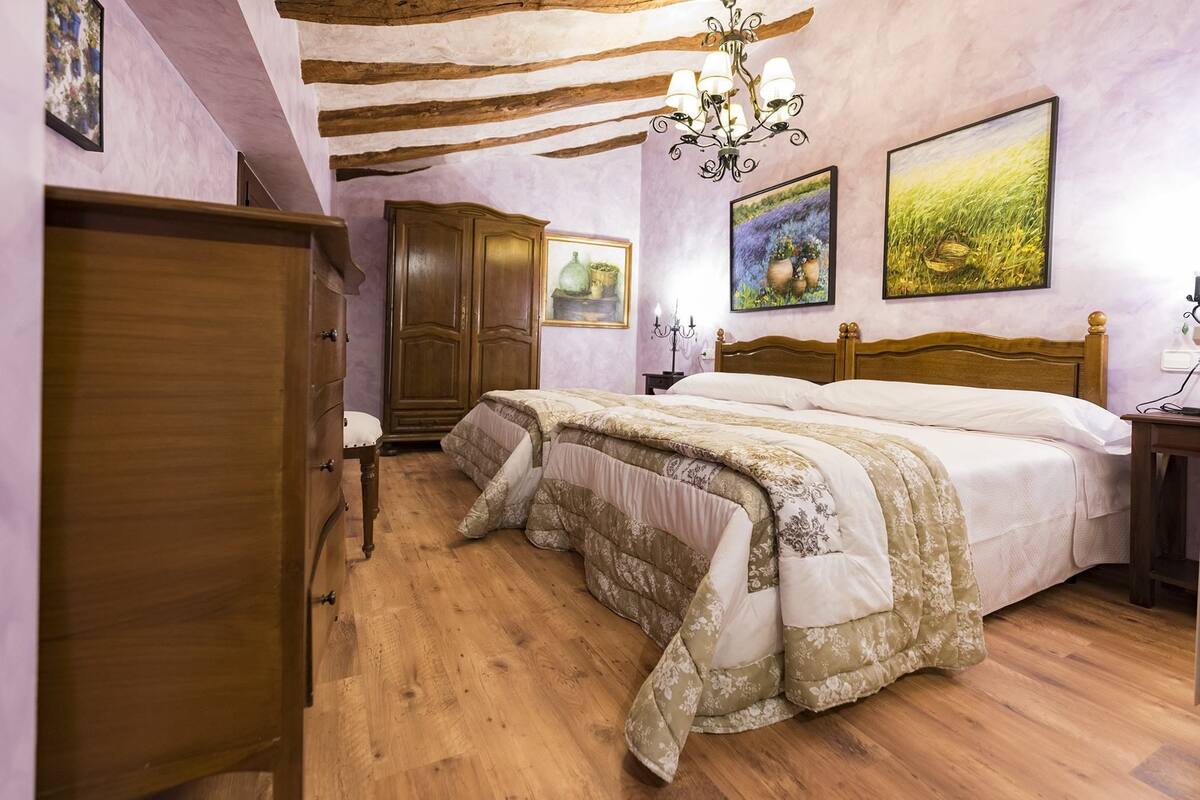 A bedroom with a wooden bed, a wooden wardrobe, a chandelier, and two framed paintings on the wall.