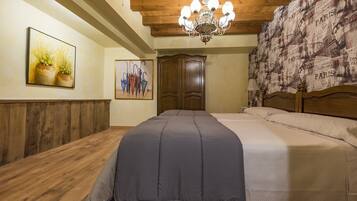 A hotel room with a wooden ceiling, a chandelier, a bed with a grey bedspread, a wooden wardrobe, and a wall with a Paris-themed wallpaper.