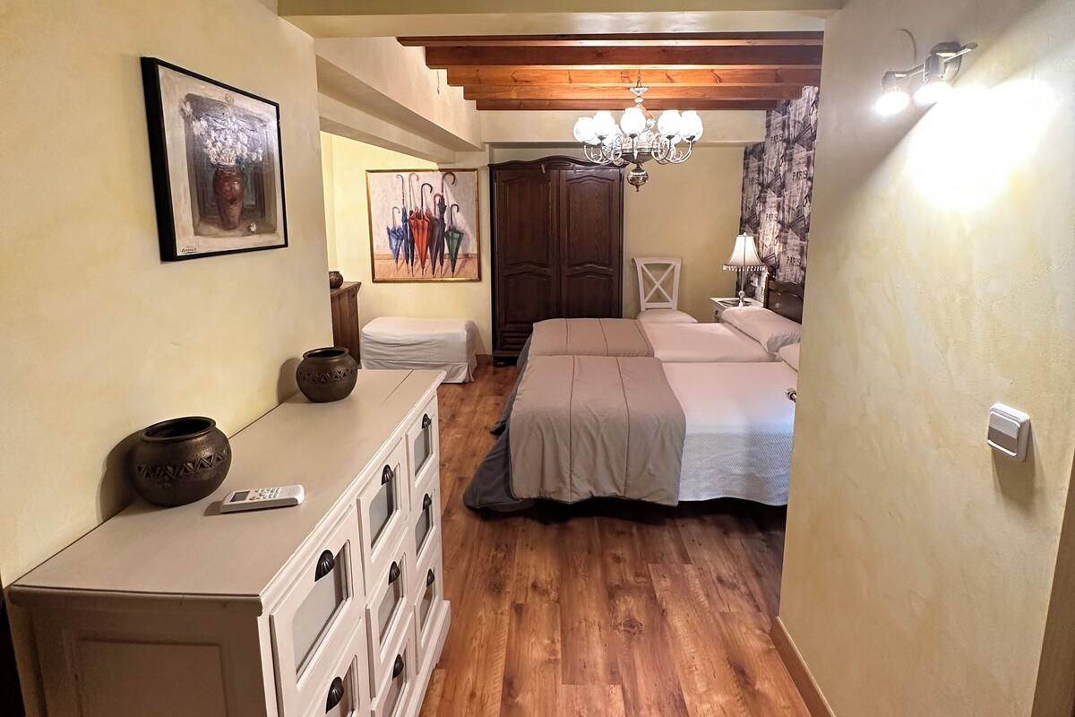 A bedroom with wooden flooring, a bed, a dresser, a mirror, and a chandelier.