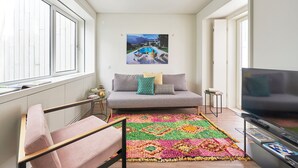 Una sala de estar moderna con un sofá, un tapete colorido, un televisor y un cuadro de un paisaje montañoso.
