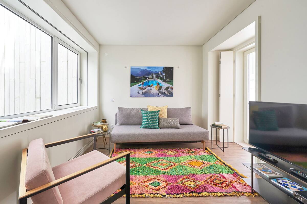 A modern living room with a sofa, a colorful rug, a television, and a painting of a mountain landscape.