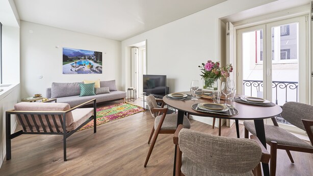 Una sala moderna con sofá, televisión, juego de comedor y una alfombra colorida.