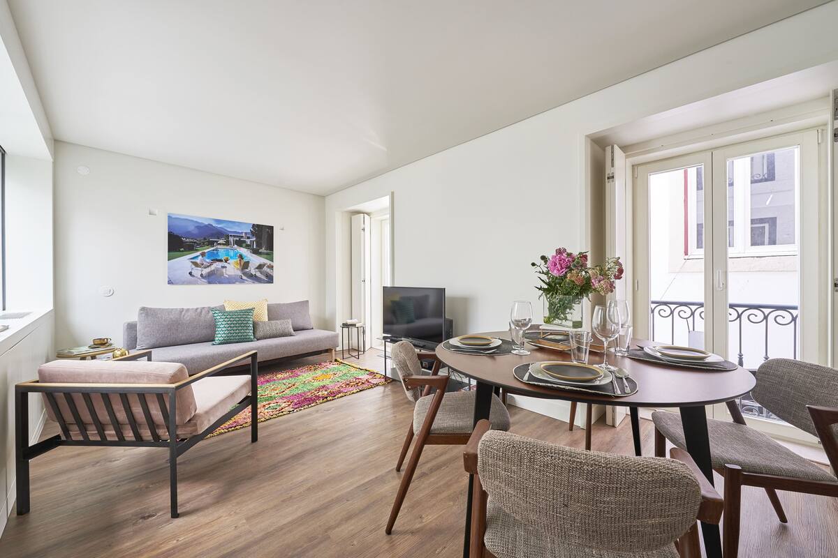 A modern living room with a sofa, TV, dining table set, and a colorful rug.