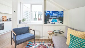 Una sala moderna con un sofá, un sillón azul, una mesita con un libro y vasos, y una alfombra colorida.