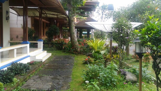 A garden pathway leading to a building with a covered porch and a small garden area with various plants and flowers. - Kota Bunga Q (Cipanas)