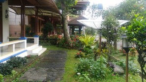 A garden pathway leading to a building with a covered porch and a small garden area with various plants and flowers. - Kota Bunga Q (Cipanas)