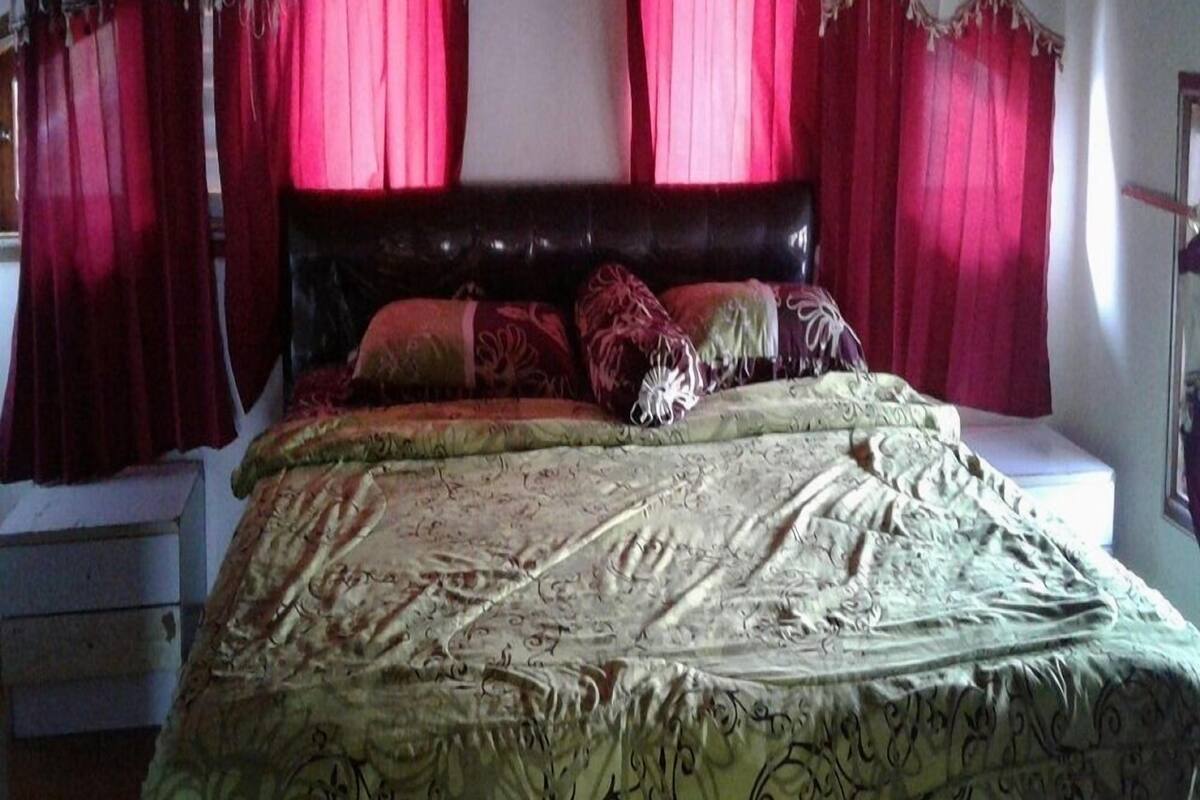 A bedroom with a large bed, a headboard, and curtains.