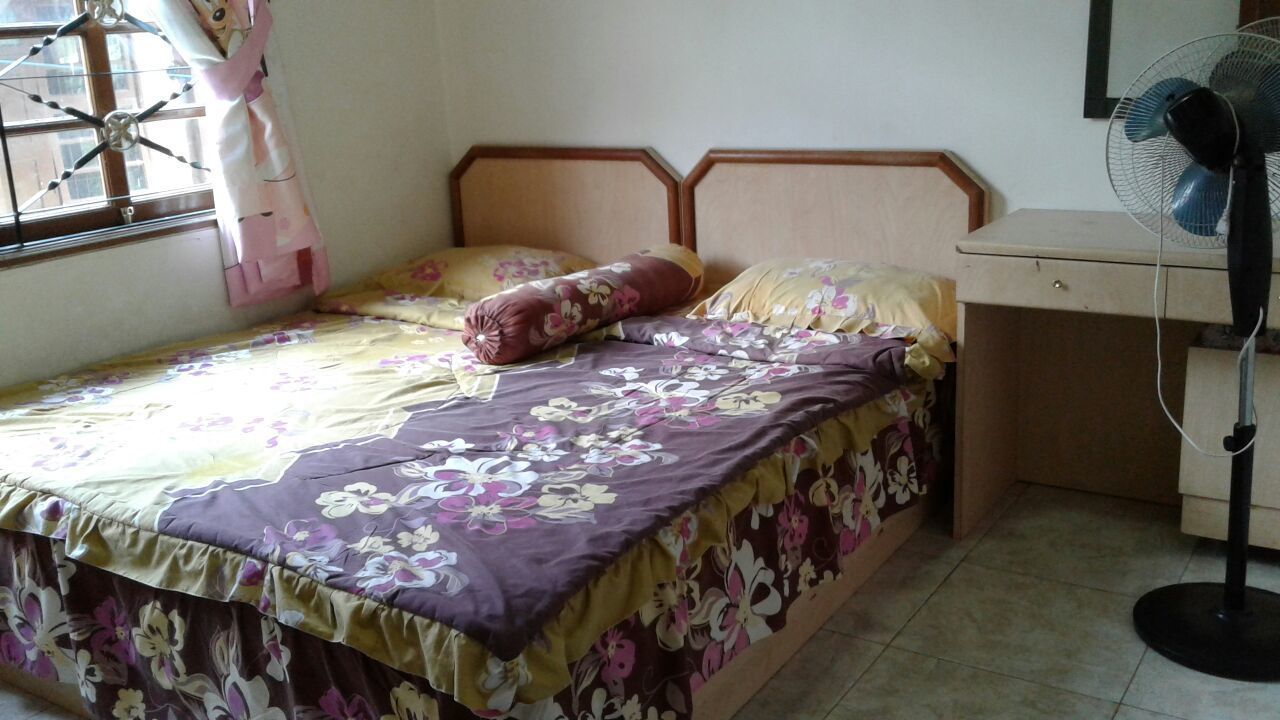 A bedroom with a bed, a window with curtains, a bedside table, and a standing fan.