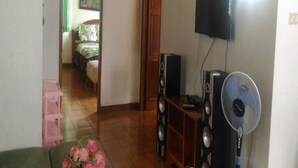 A living room with a TV mounted on the wall, a fan, and a speaker system. - Kota Bunga Q (Cipanas)
