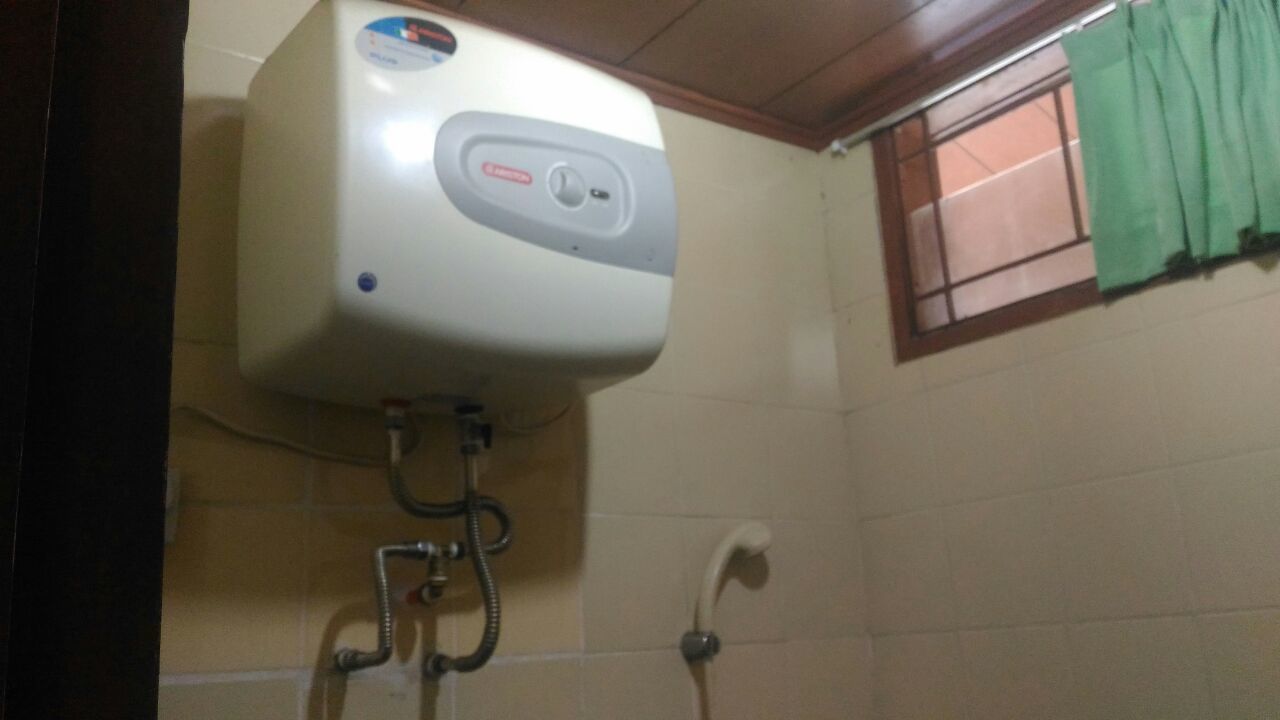 A bathroom with a hand dryer mounted on the wall, a window with a green curtain, and a tiled floor.