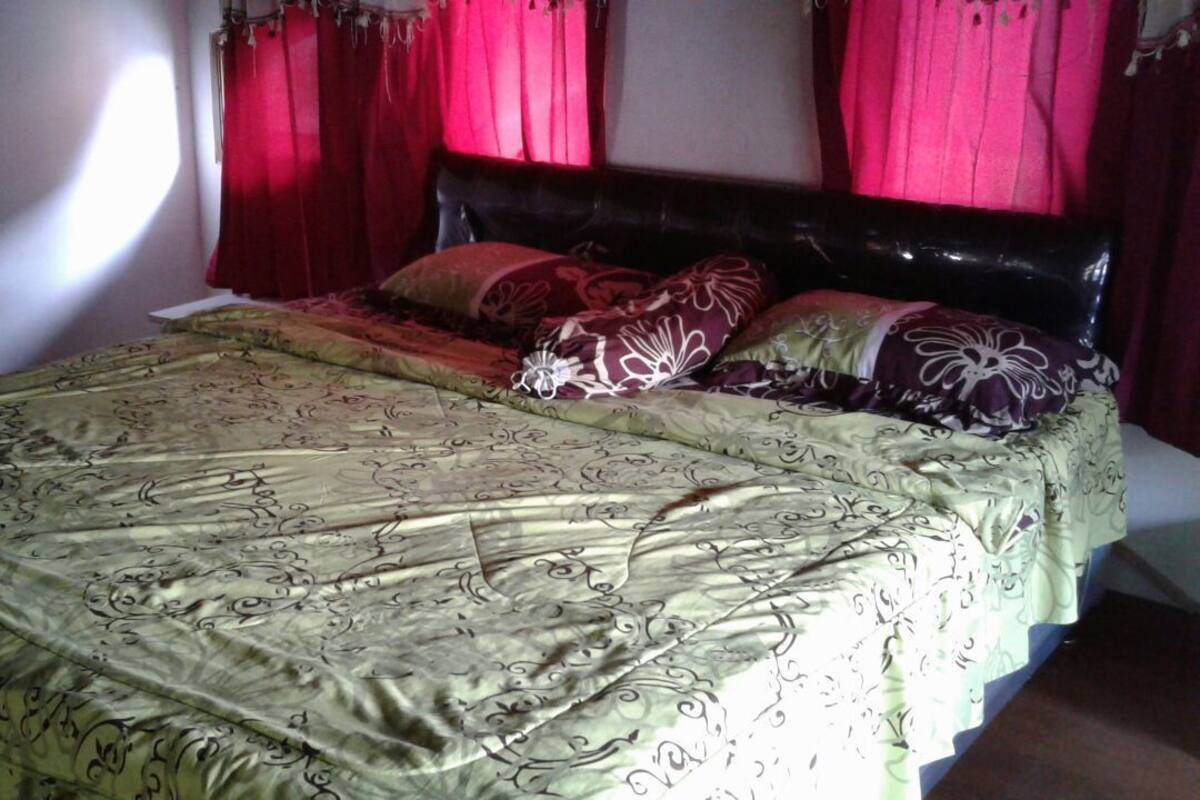 A bed with a patterned bedspread and multiple pillows, red curtains, and a dark headboard.