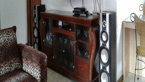 A living room with a wooden cabinet, a television mounted on the wall, and a pair of speakers. - Kota Bunga Q (Cipanas)