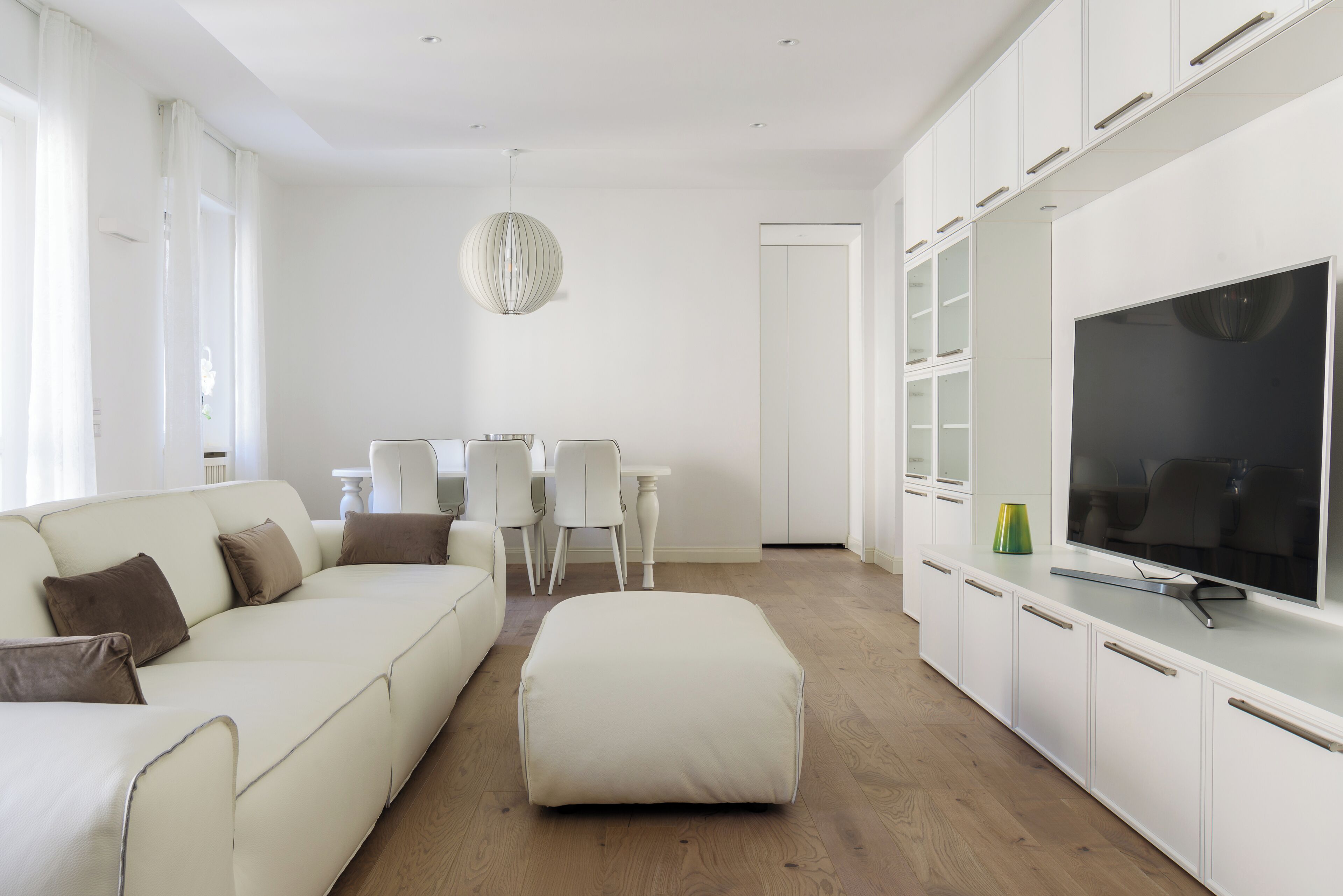 A modern living room with a sofa, ottoman, TV, and white cabinets.