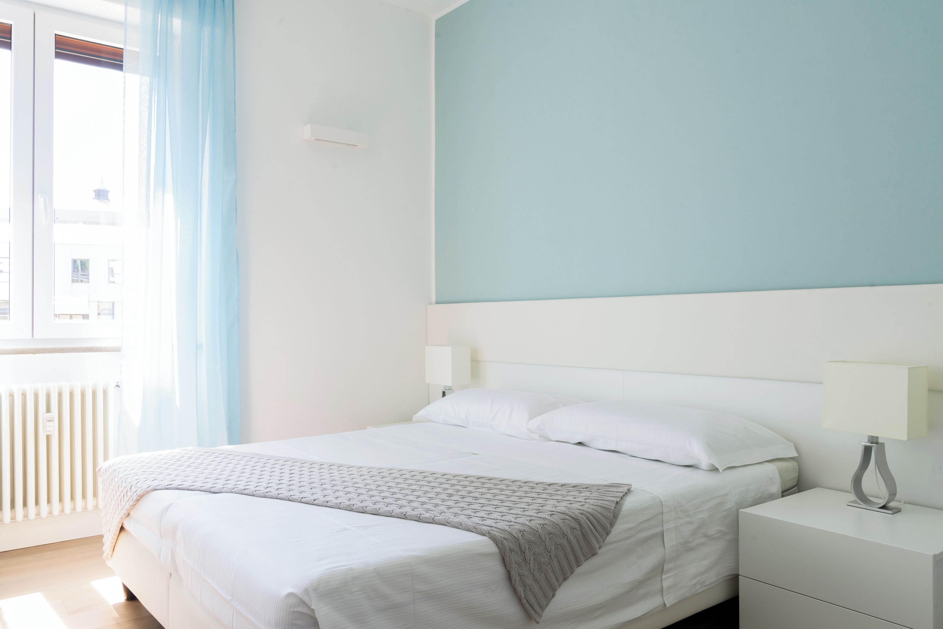 A bedroom with a bed, bedside tables, a window with curtains, and a radiator.