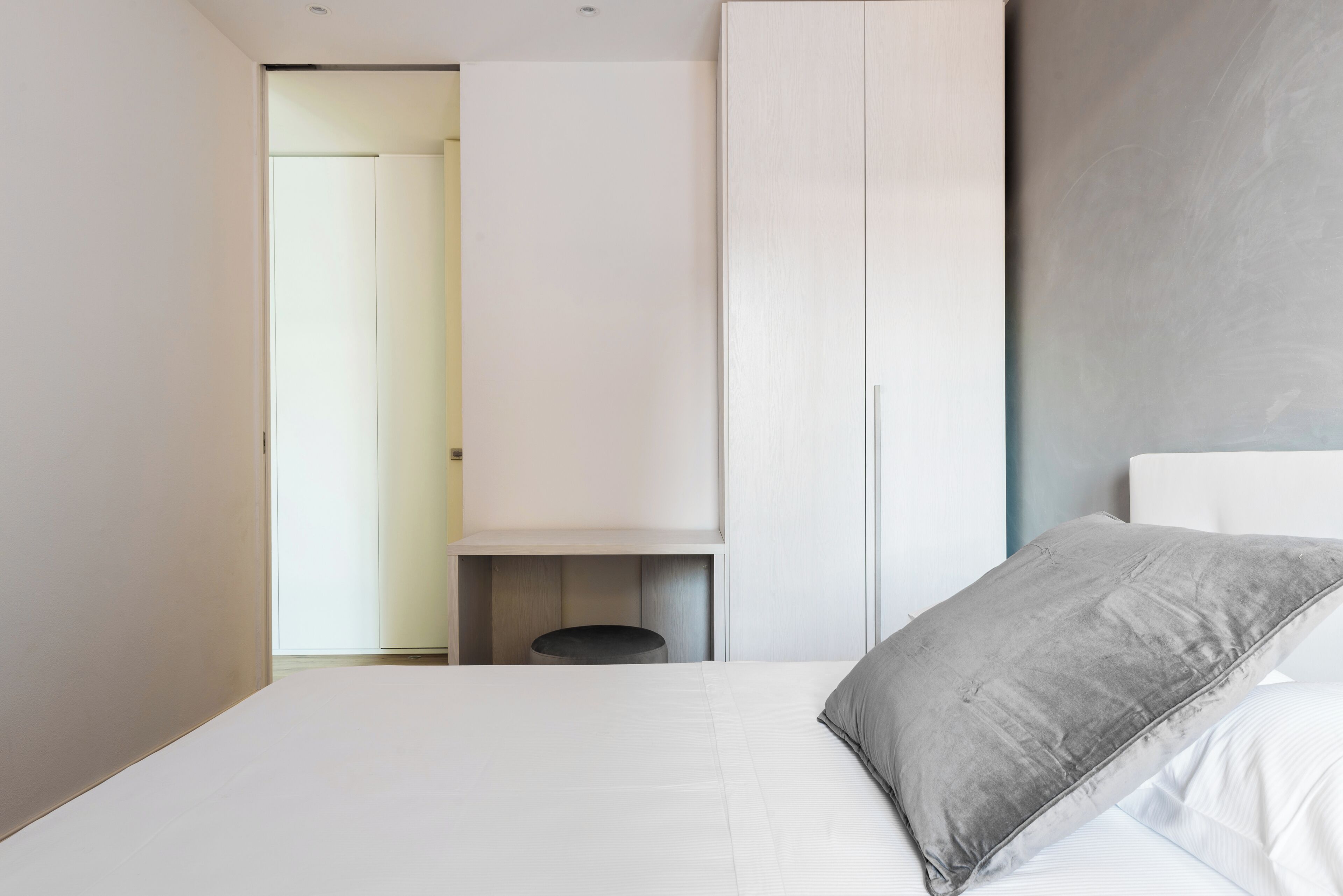 A bedroom with a bed, a grey pillow, a white wardrobe, and a small round table.