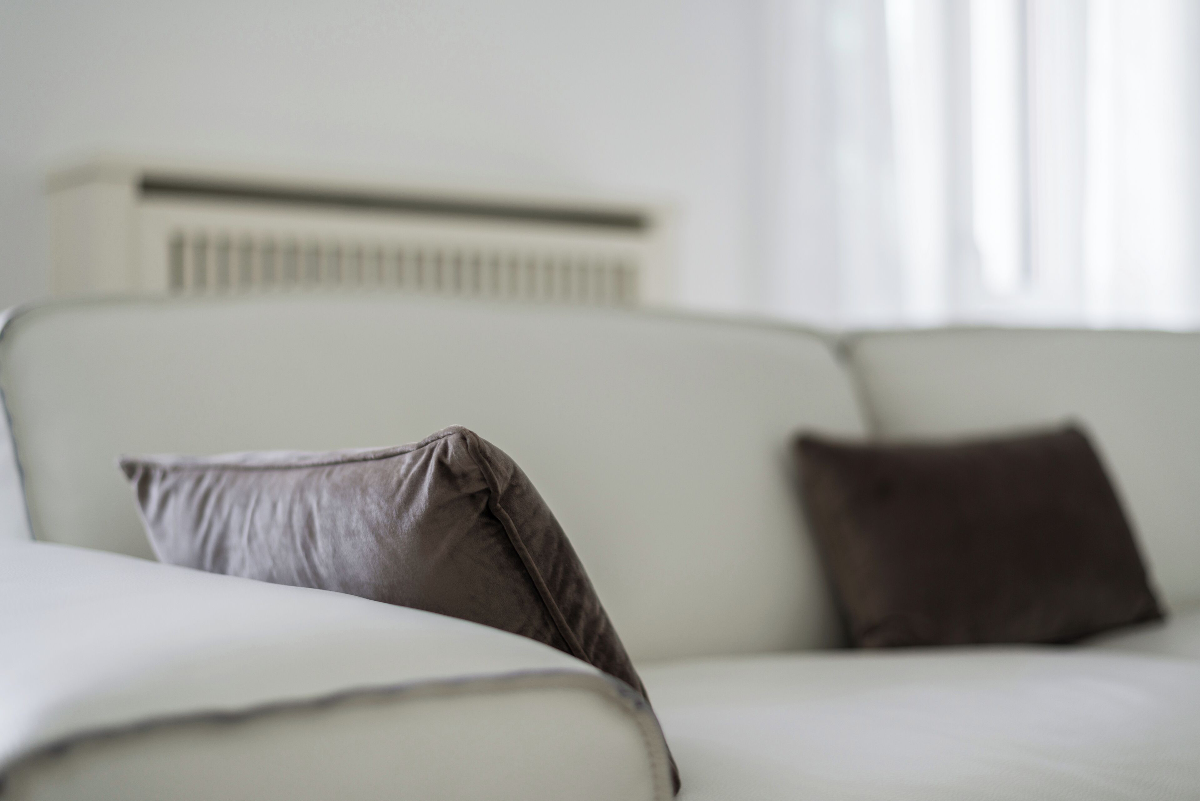 Un sofá blanco con dos almohadas, una pared blanca y una ventana con persianas.