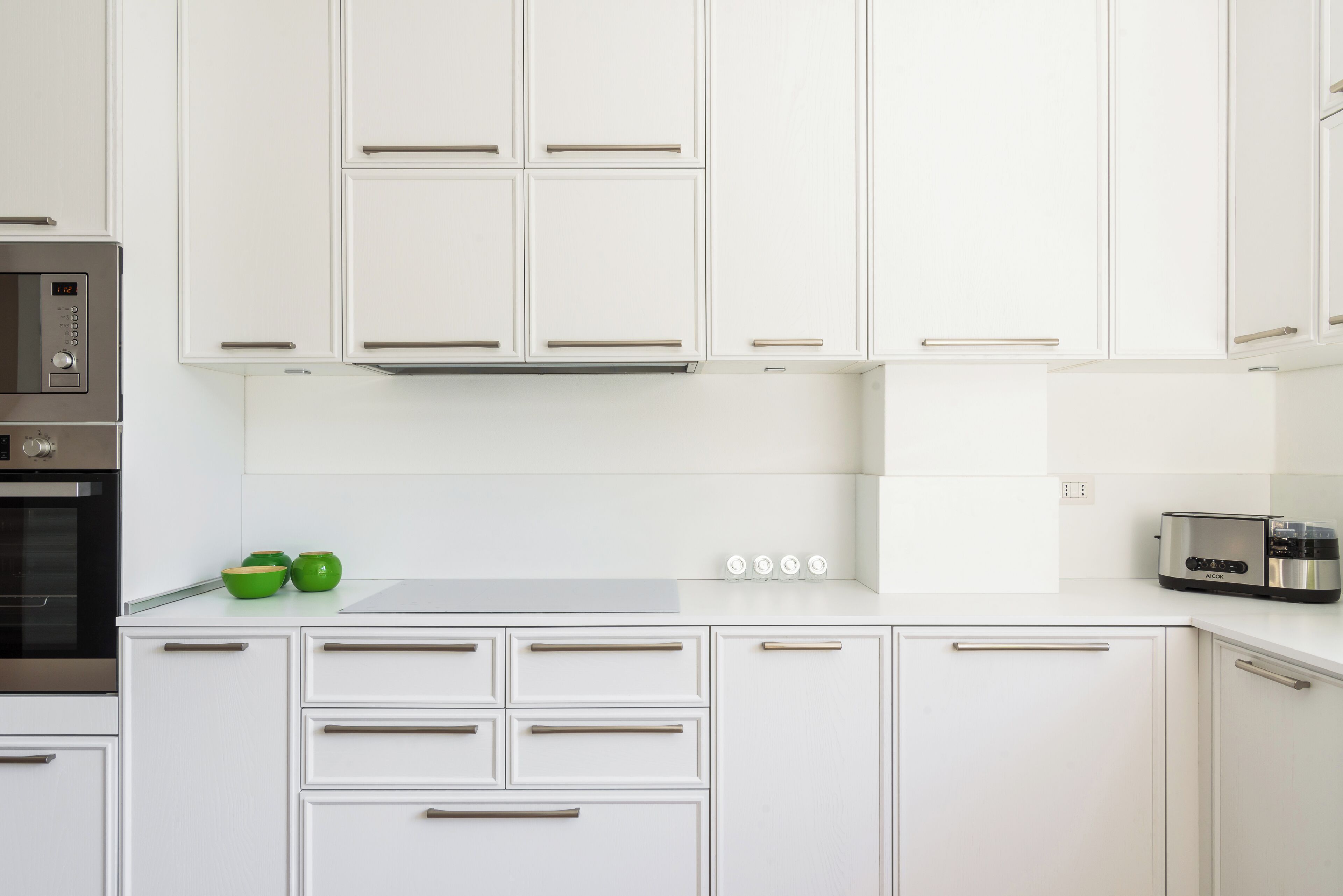 Une cuisine moderne avec des meubles blancs, un four encastré, un four à micro-ondes et un grille-pain.
