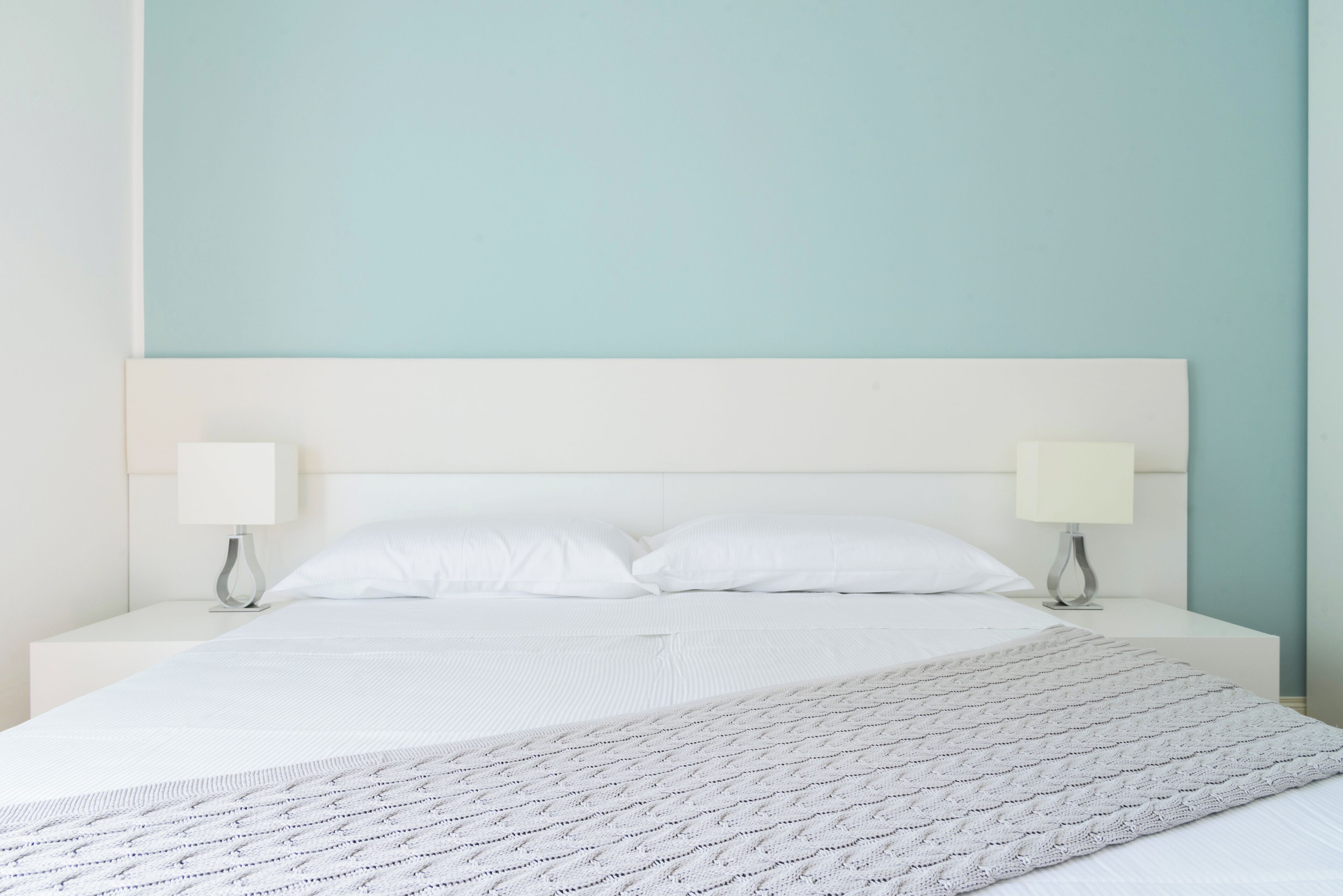 A bed with white linens, two bedside lamps, and a light blue wall.