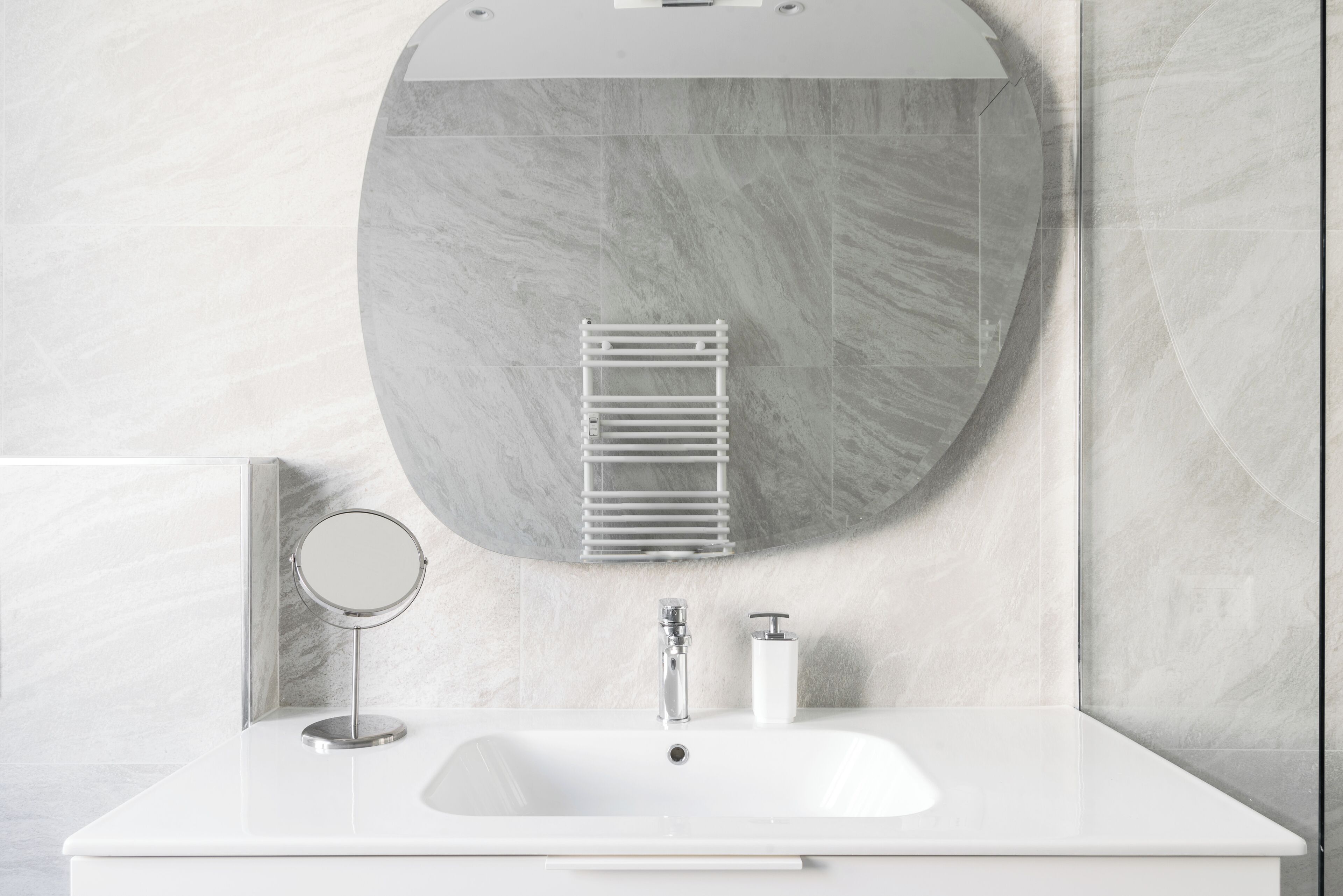 A bathroom with a white sink, a round mirror, a towel rack, and a wall-mounted toilet paper holder.