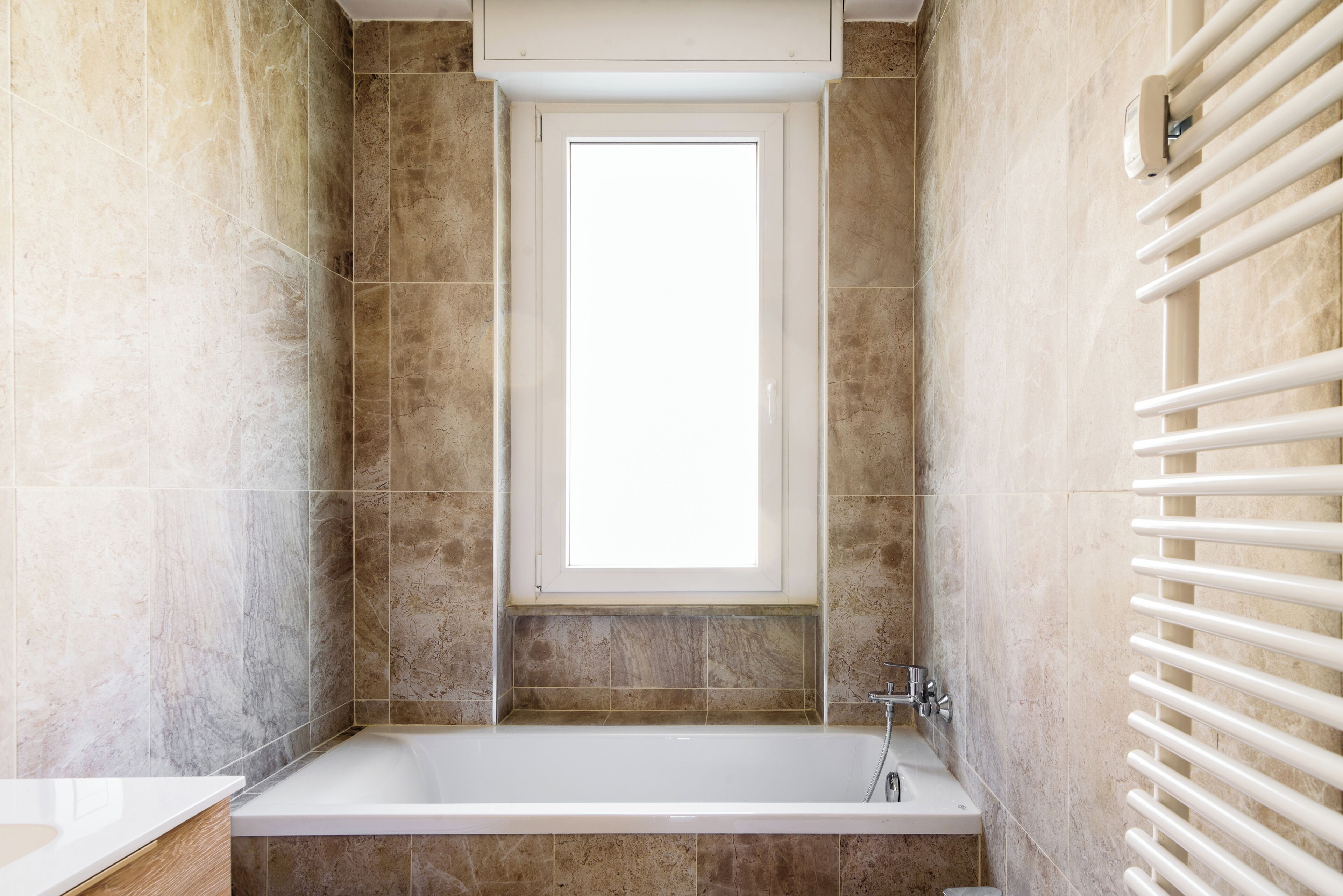 A bathroom with a bathtub, a window, and a white towel rack.