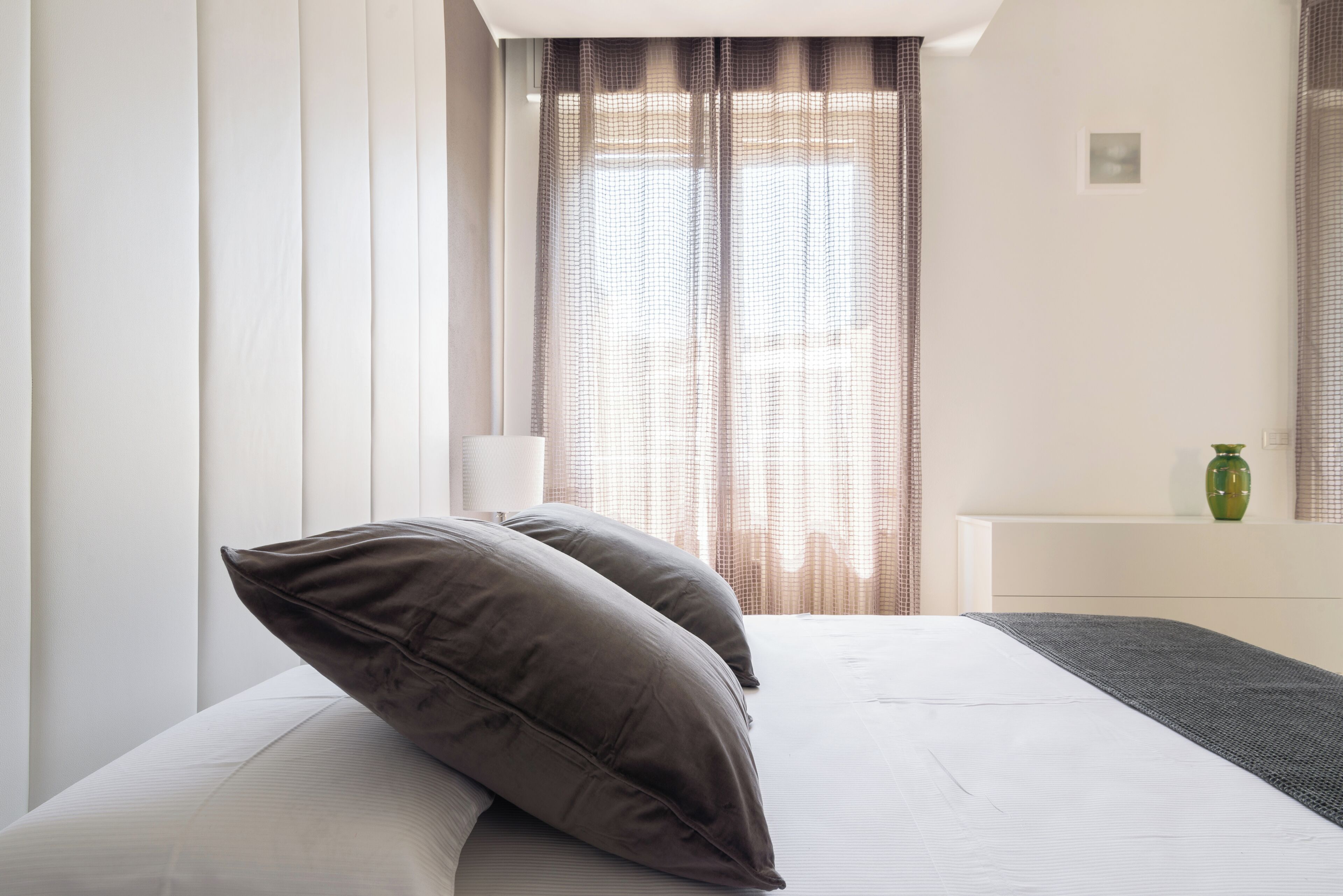 A hotel room with a bed, a nightstand, a lamp, and a window with curtains.