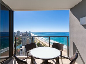 A balcony with a table and chairs overlooking a beach and cityscape.