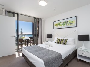 A hotel room with a bed, bedside tables, a view of the ocean, and a painting on the wall.