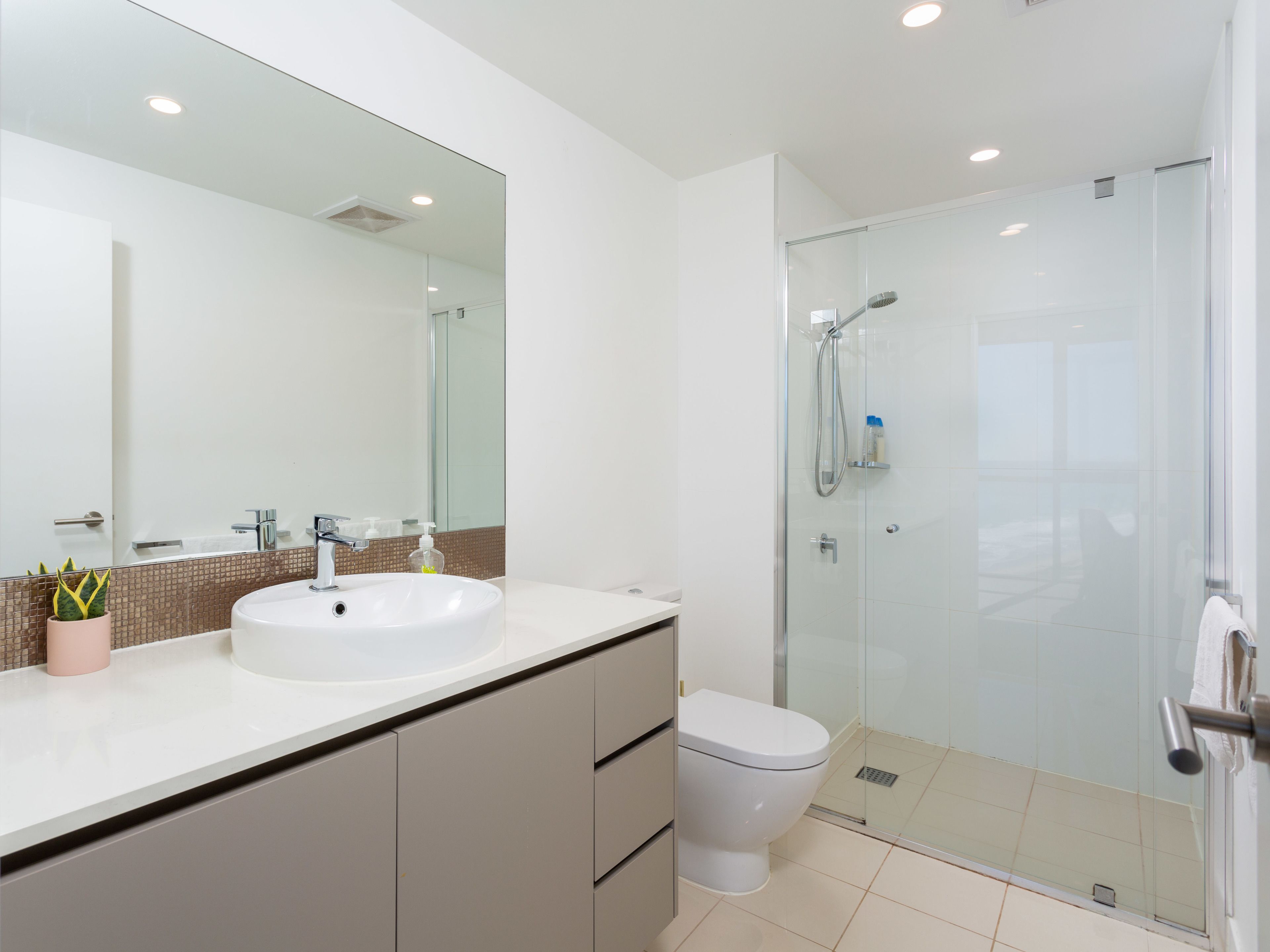 Een moderne badkamer met een witte wastafel, een douchecabine van glas en een toilet.