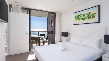 A hotel room with a bed, a painting, a nightstand, a lamp, and a view of the ocean.