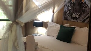 A bed with a white bedspread, a green pillow, and a white pillow. There is a lamp on a bedside table. - Oveng Lodge (Nkolmétet)