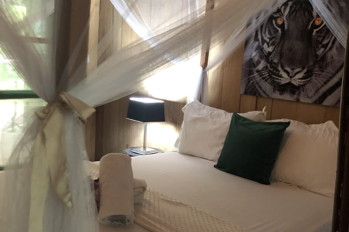 A bed with a white bedspread, a green pillow, and a white pillow. There is a lamp on a bedside table.