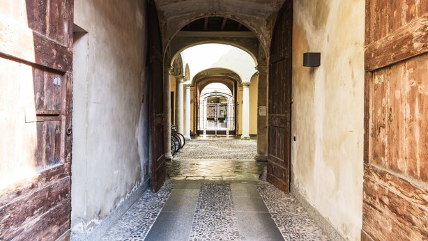 A corridor with wooden doors and arches, leading to a gated area.