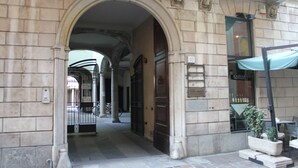 A stone building entrance with an arched doorway, a small outdoor seating area with a table and chairs, and a sign indicating the number 10.