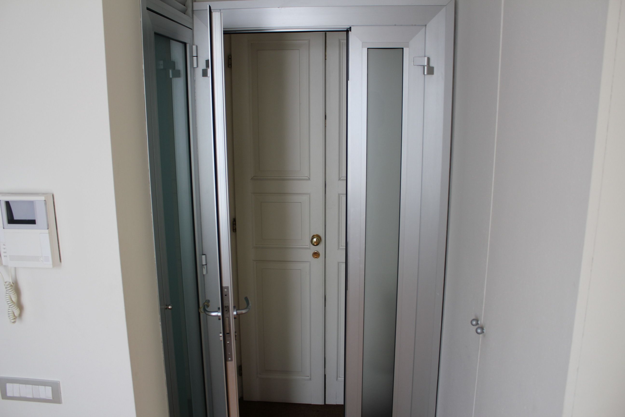 A white door with a brass doorknob, a wall-mounted intercom, and a light switch.