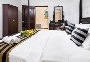 A hotel room with a bed, a wardrobe, a desk with a mirror, and a painting on the wall.