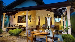 A covered outdoor seating area with tables and chairs, a small garden, and a building entrance. - Grand Conch Villa (Tangalle)